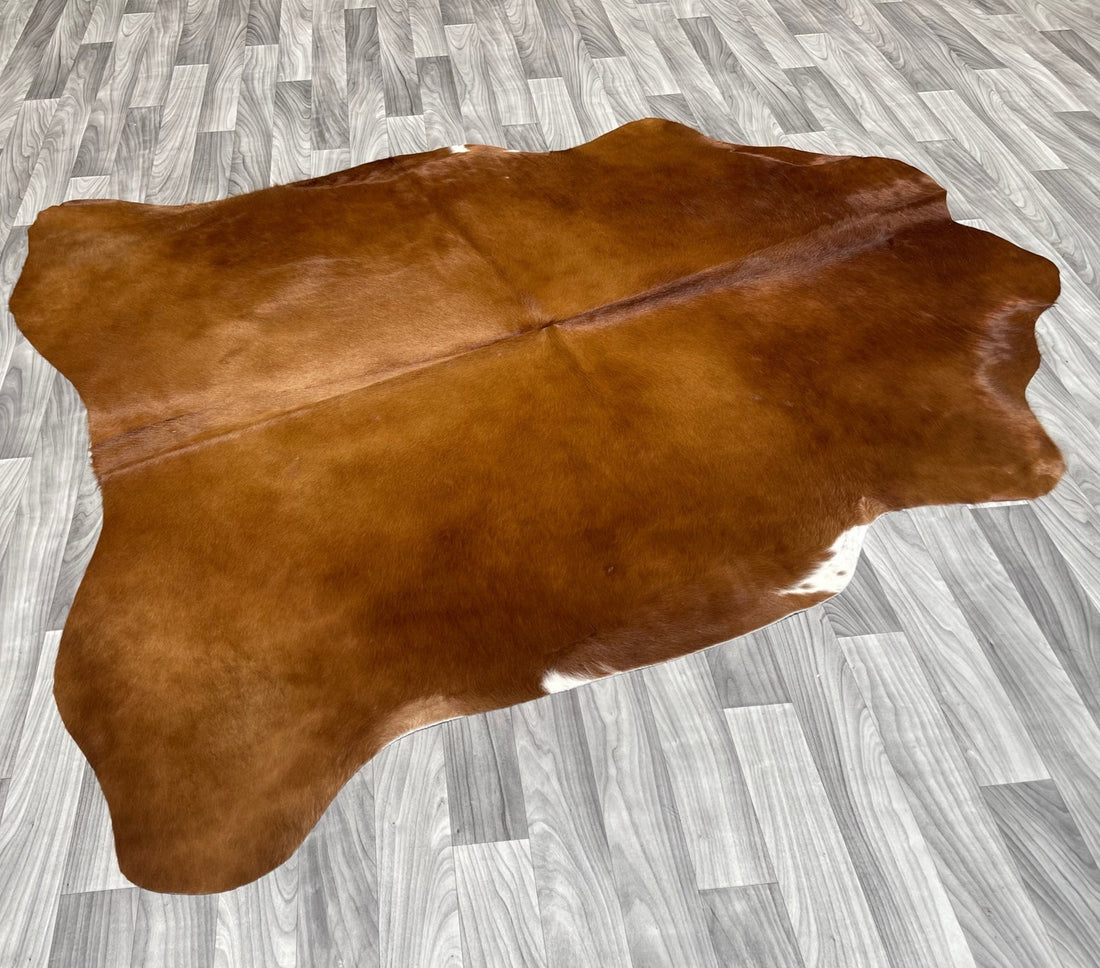 A brown cowhide rug on a grey wooden floor